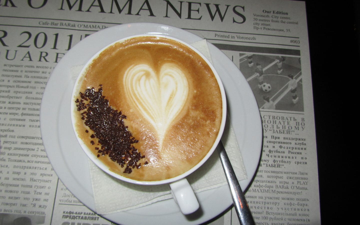 Cappuccino with heart latte art and chocolate shavings on a newspaper