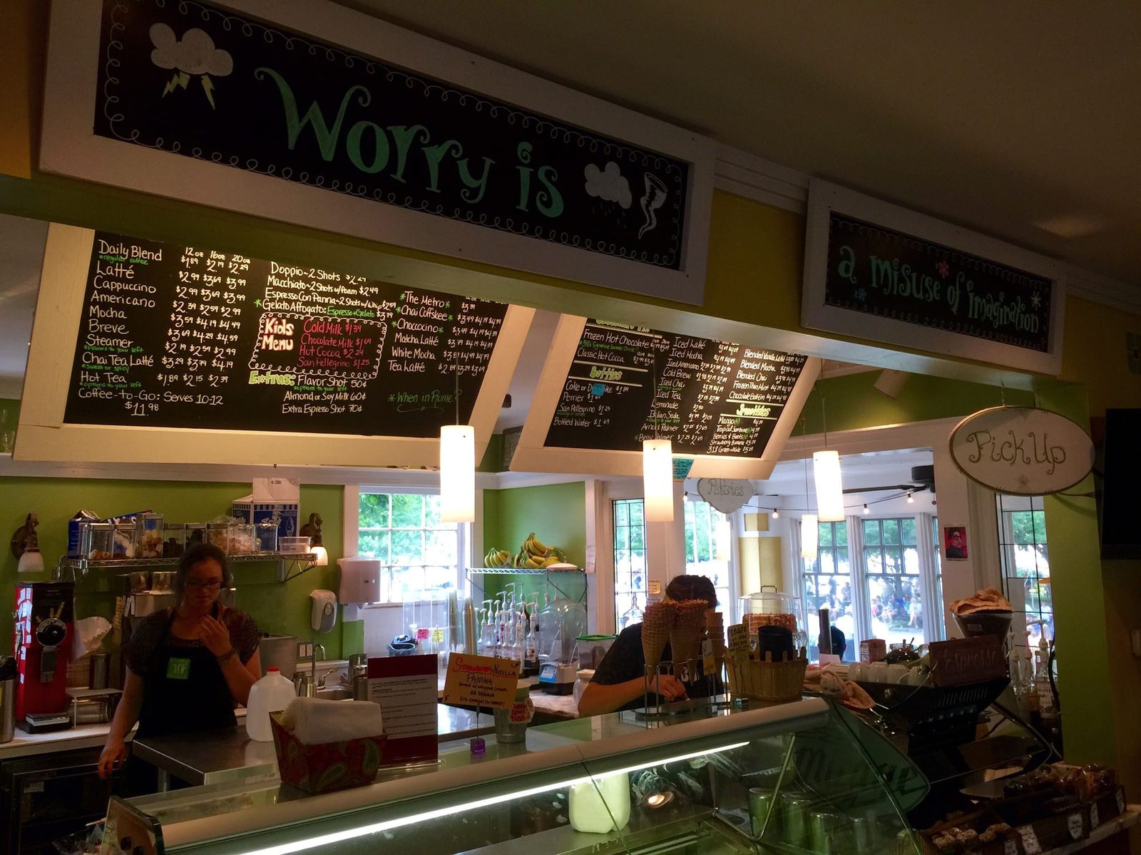 Green cafe counter with chalkboard menus, baristas and a pastry case
