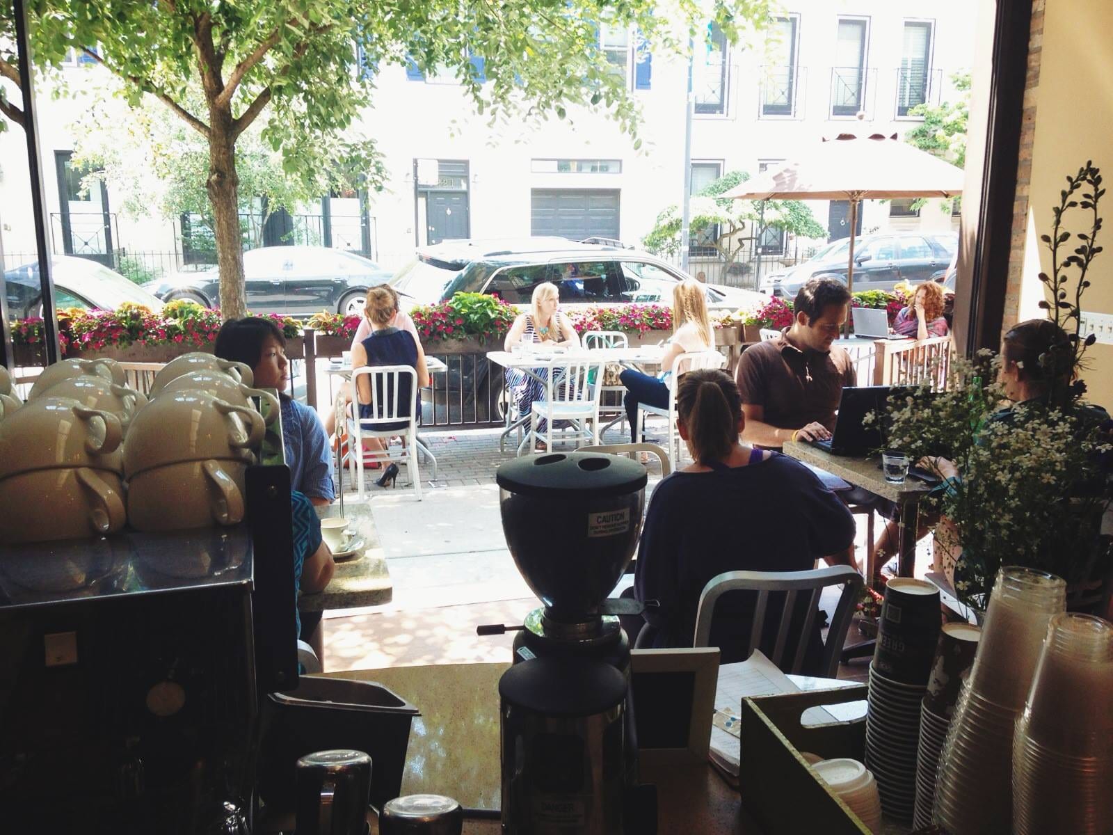 View past grinder and stacked cups to sunny sidewalk patio