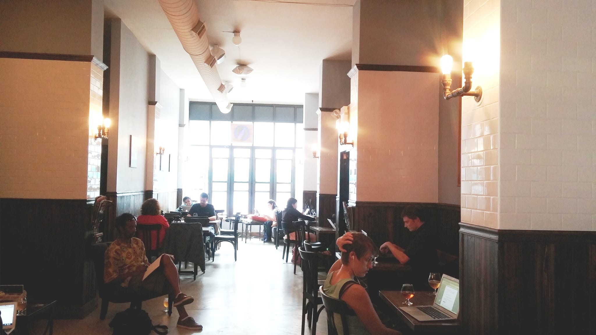 Tall tiled cafe room with tables of people reading and using laptops