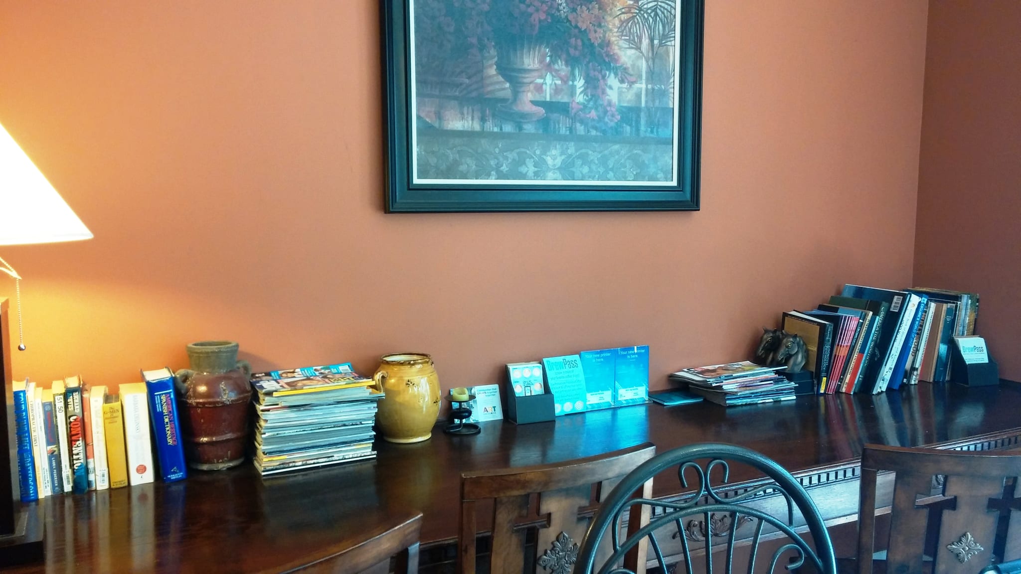 Wooden sideboard stacked with books and magazines against a terracotta wall