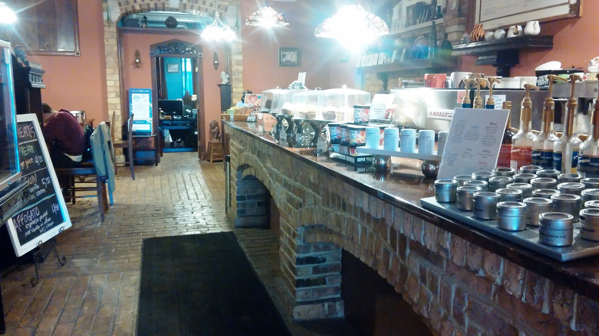 Long brick-fronted counter with tea tins, syrup bottles and espresso machine