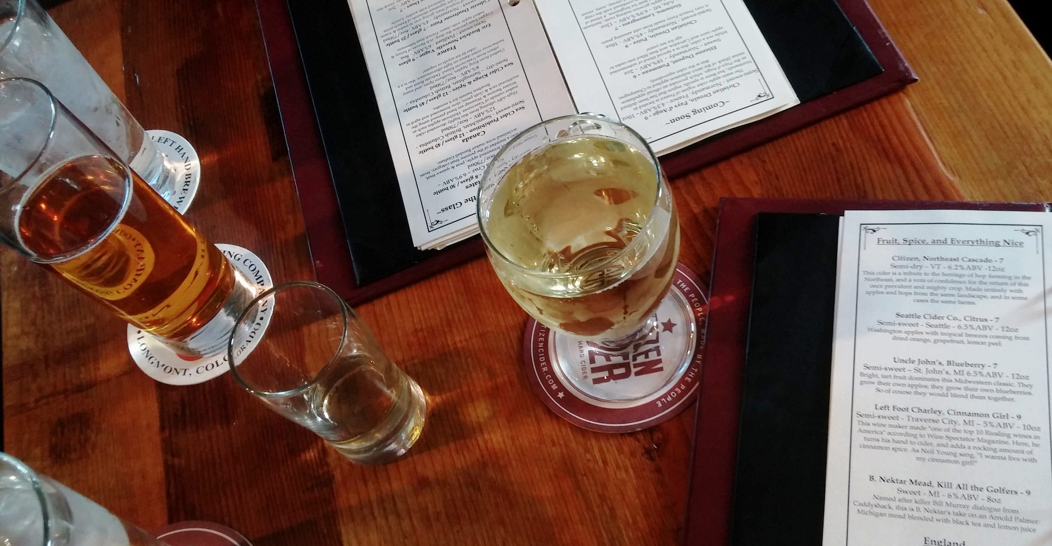 Glasses of cider on a wooden table beside printed cider menus