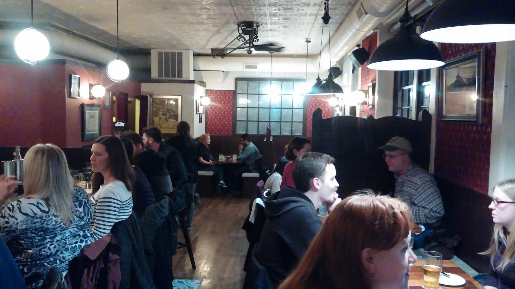 Crowded pub dining room with globe pendants, tin ceiling and red wallpaper
