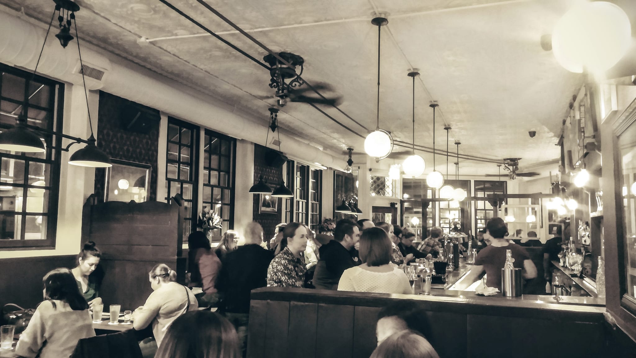 Sepia view of a busy bar and dining room under hanging globe lamps