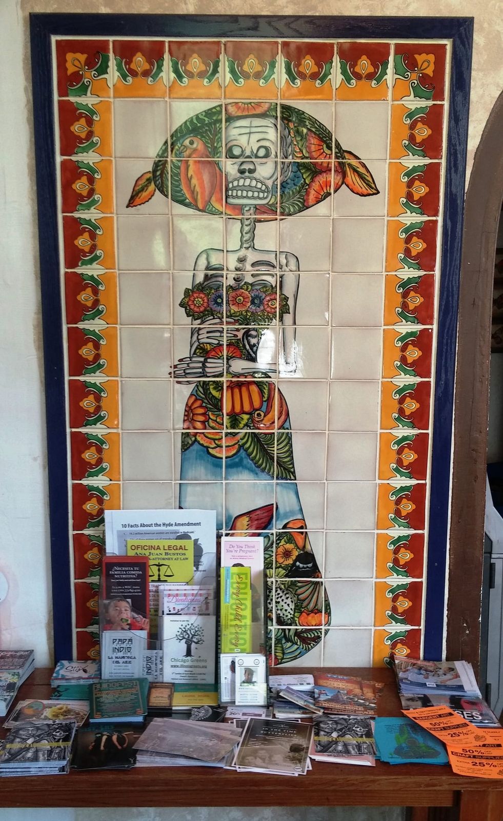 Tiled mural of a flower-hatted skeleton above a table of flyers