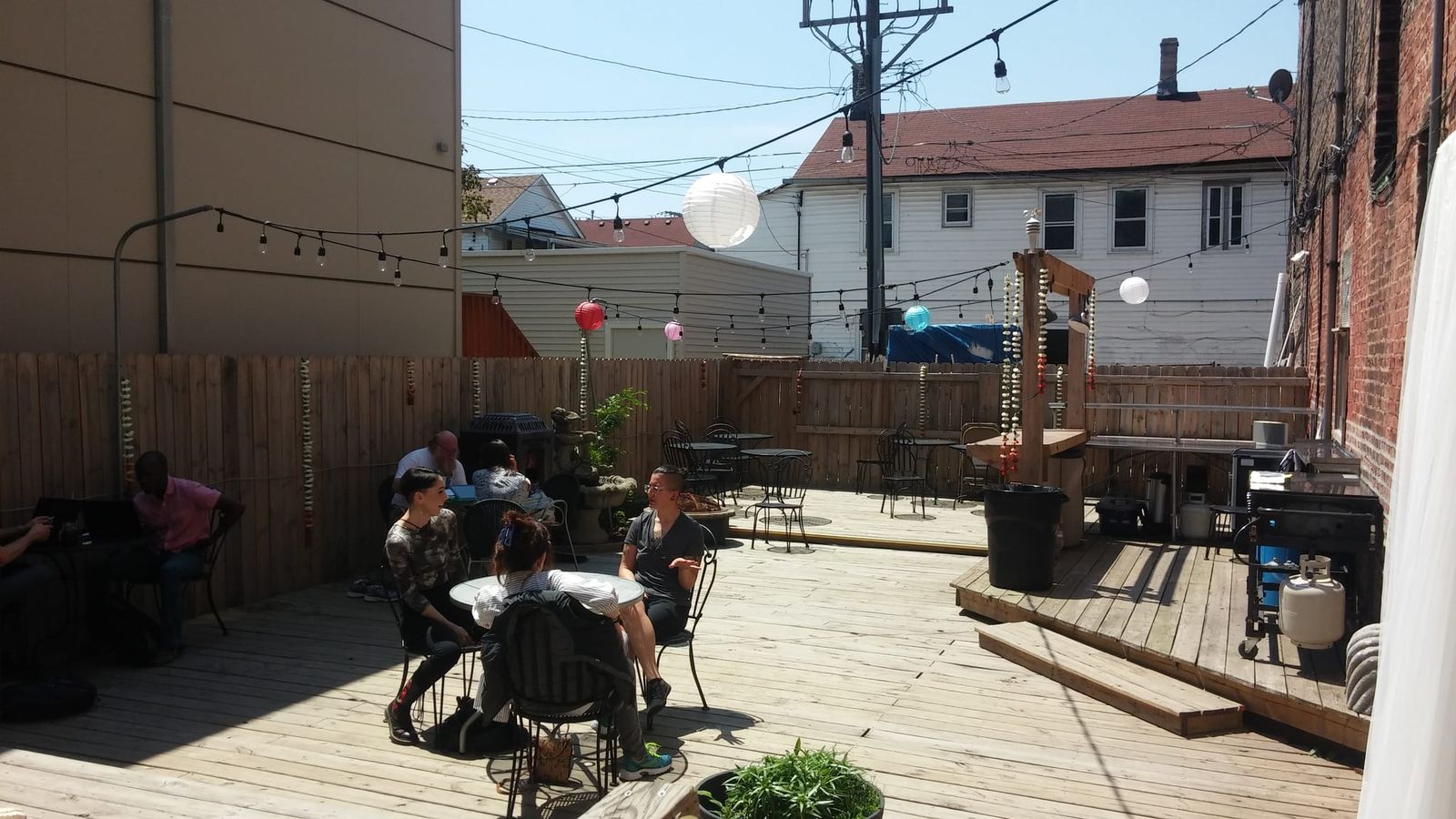 Sunny wooden back patio with cafe tables, string lights and paper lanterns