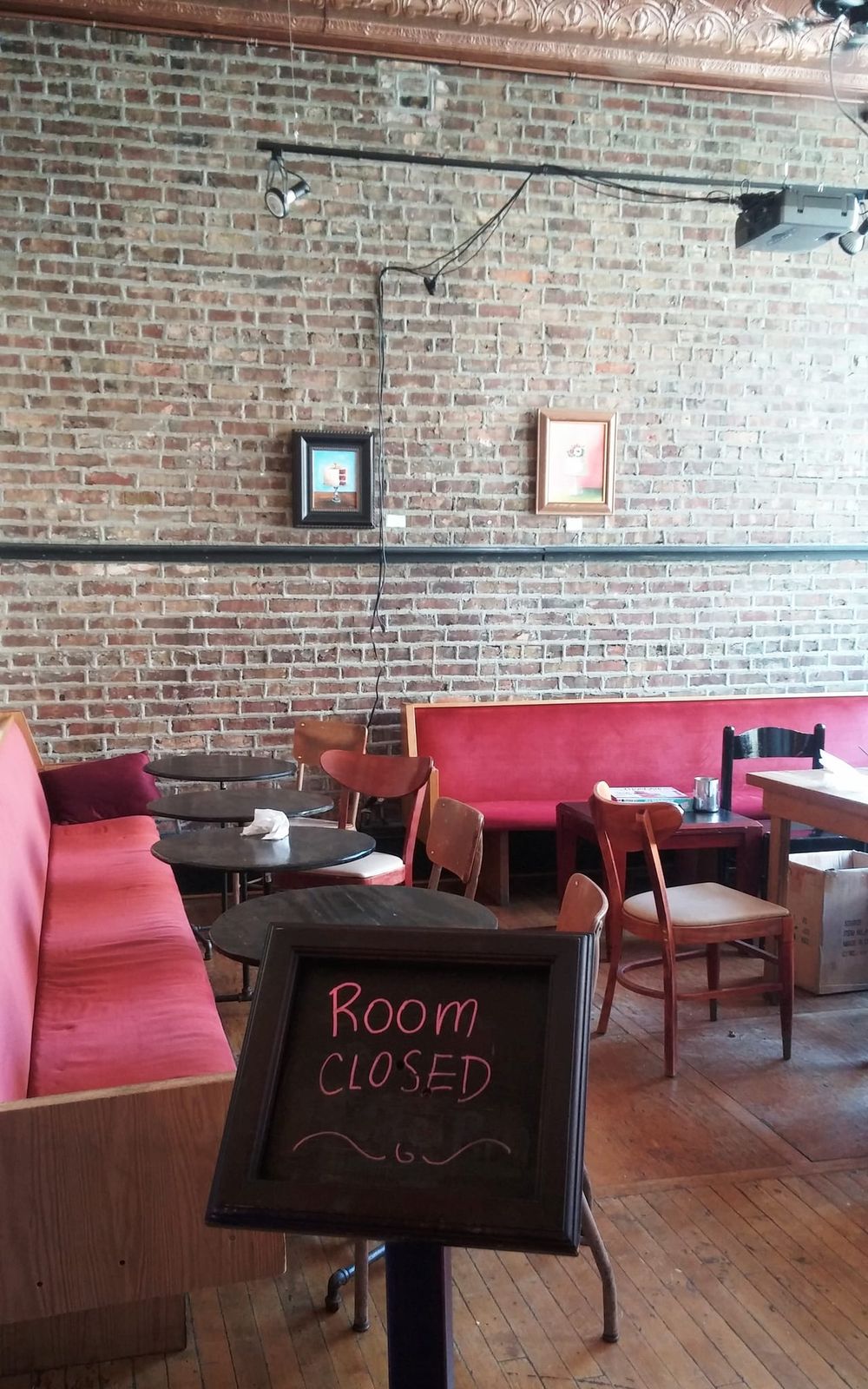 Exposed brick back room with pink banquettes and a Room Closed chalkboard
