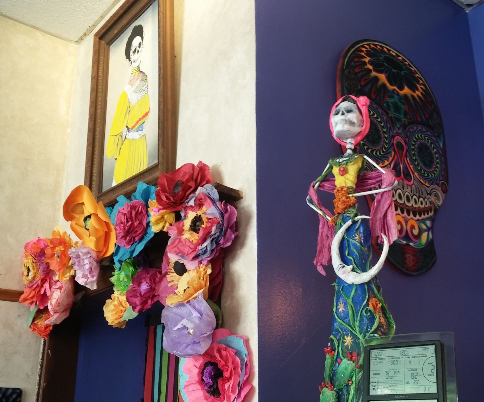 Paper flowers, a skeleton figure and sugar skull art on purple walls