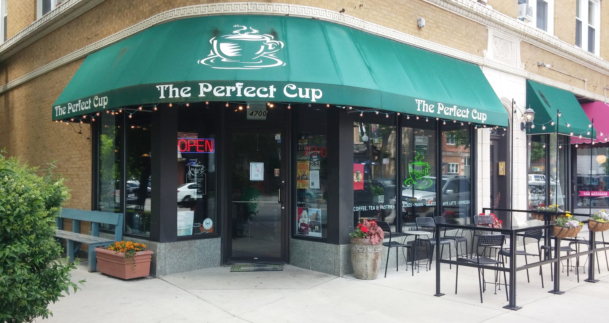 Corner coffeehouse with green awning, sidewalk tables and neon Open sign