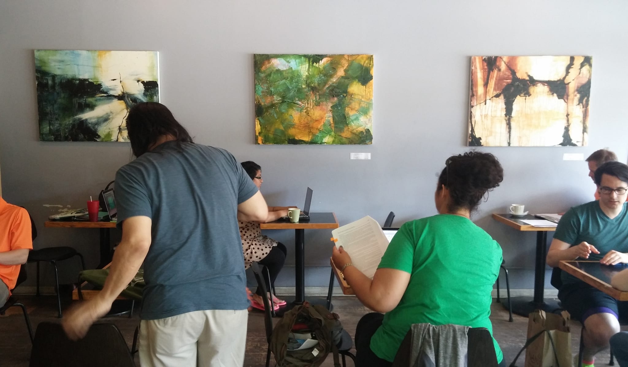 People working at cafe tables below three large abstract paintings