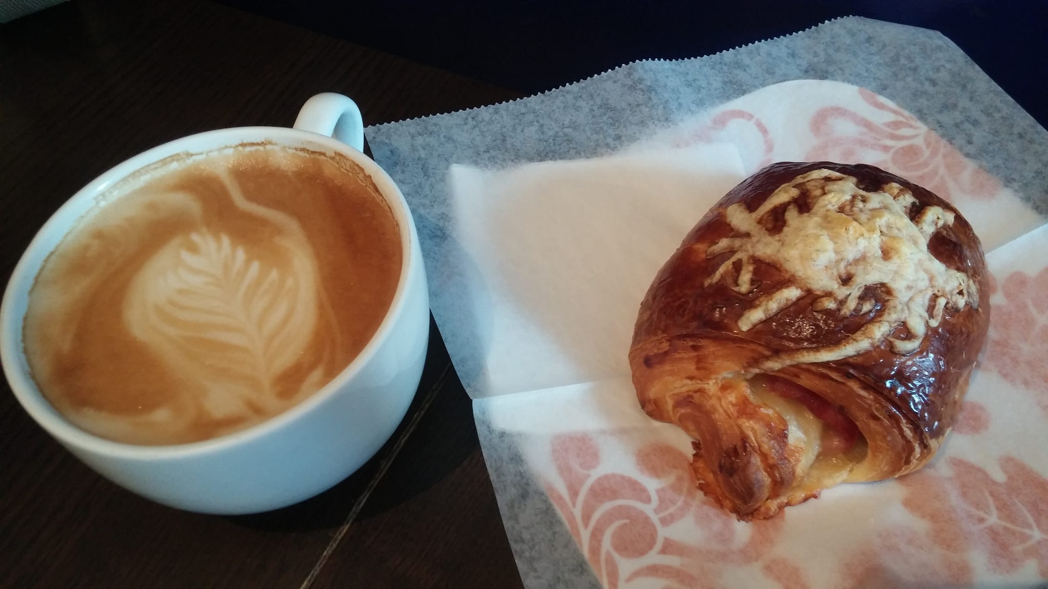Latte with rosetta art beside a ham and cheese croissant