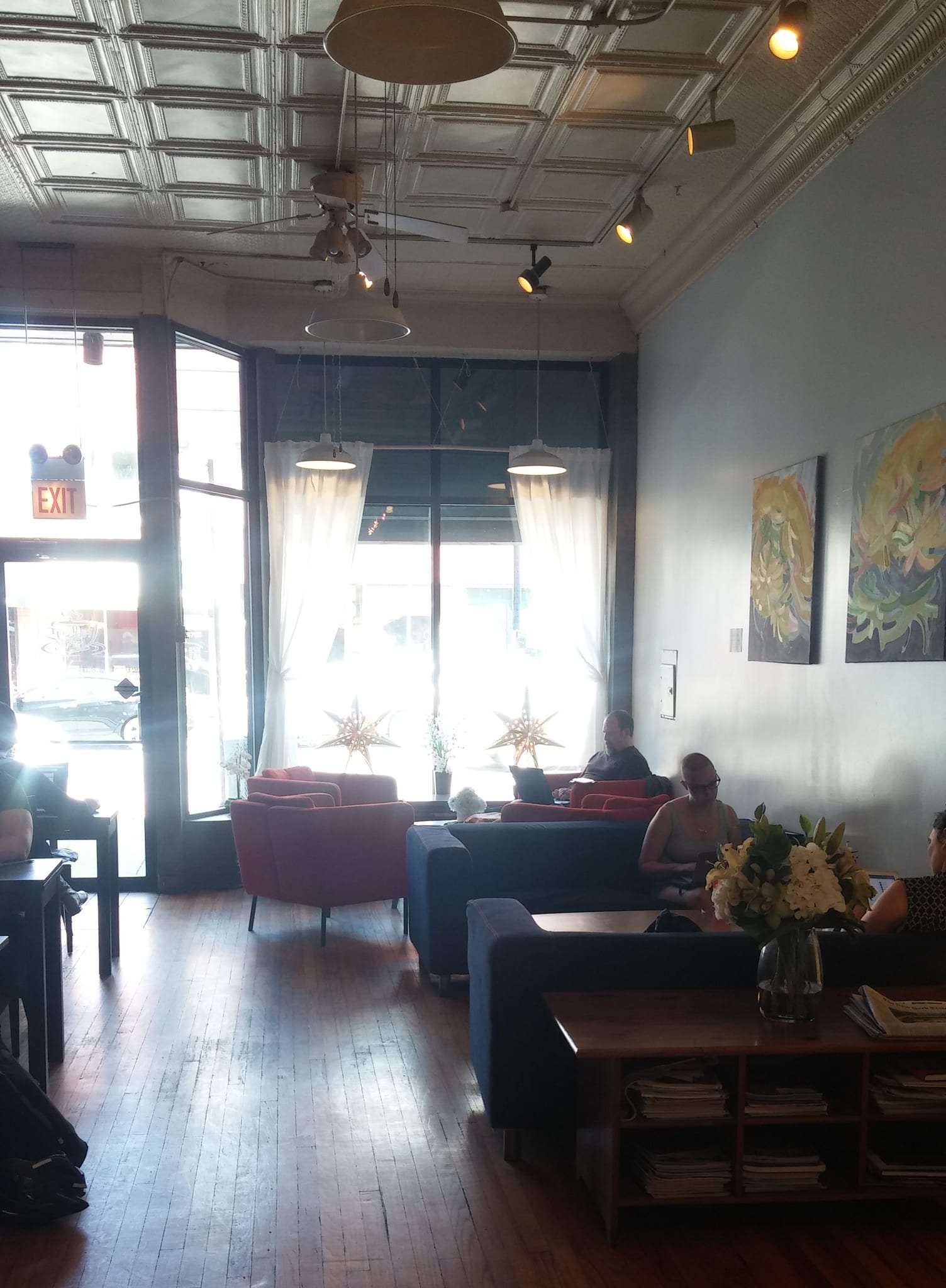 Sunlit lounge with red and blue armchairs under a pressed tin ceiling