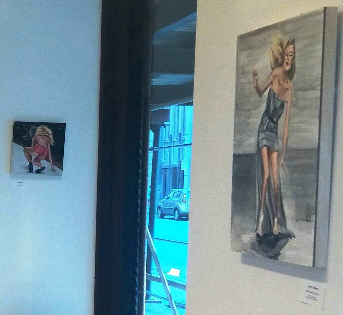 Two figurative paintings flanking a window on pale gallery walls
