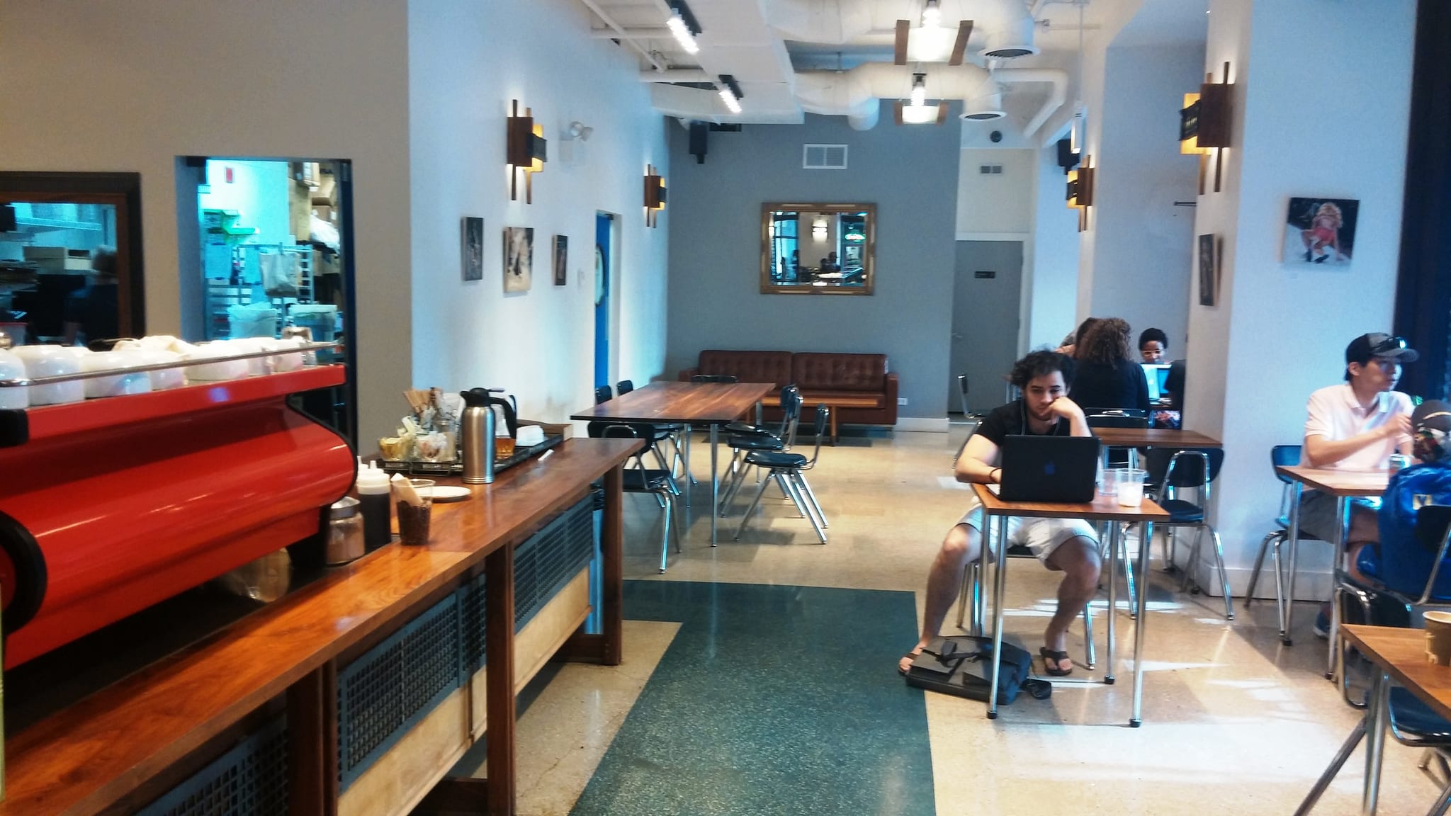 Bright cafe with red espresso machine, school chairs and laptop workers