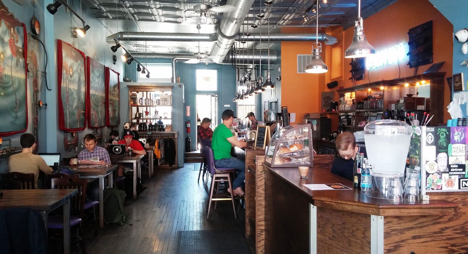 Long narrow cafe with murals, wood tables and a pastry case at the bar