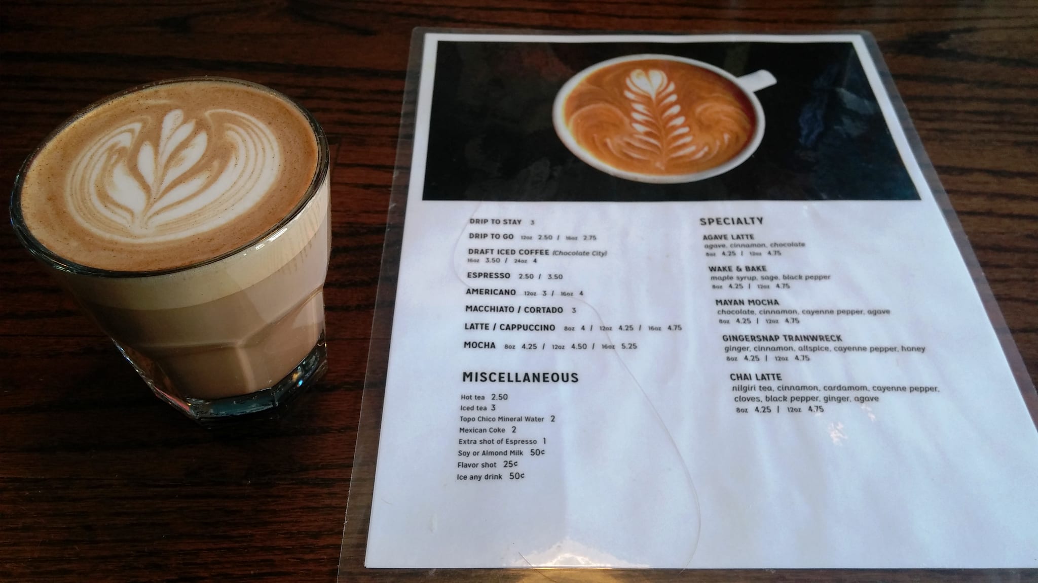 Latte in a glass tumbler next to a printed drink menu