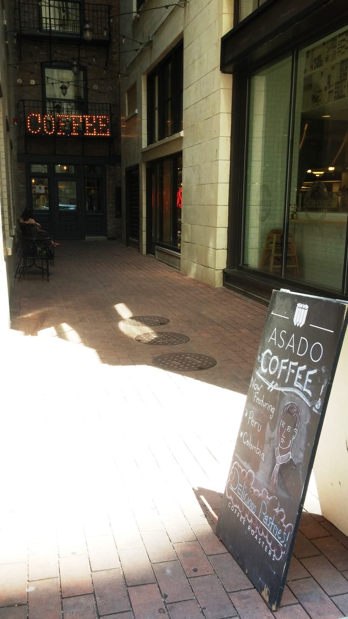 Brick alley entrance with lit COFFEE marquee and Asado chalkboard sign