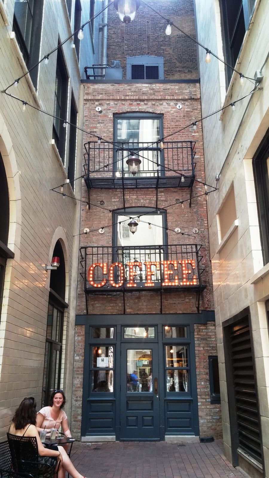 Narrow alley courtyard with string lights and glowing COFFEE marquee sign
