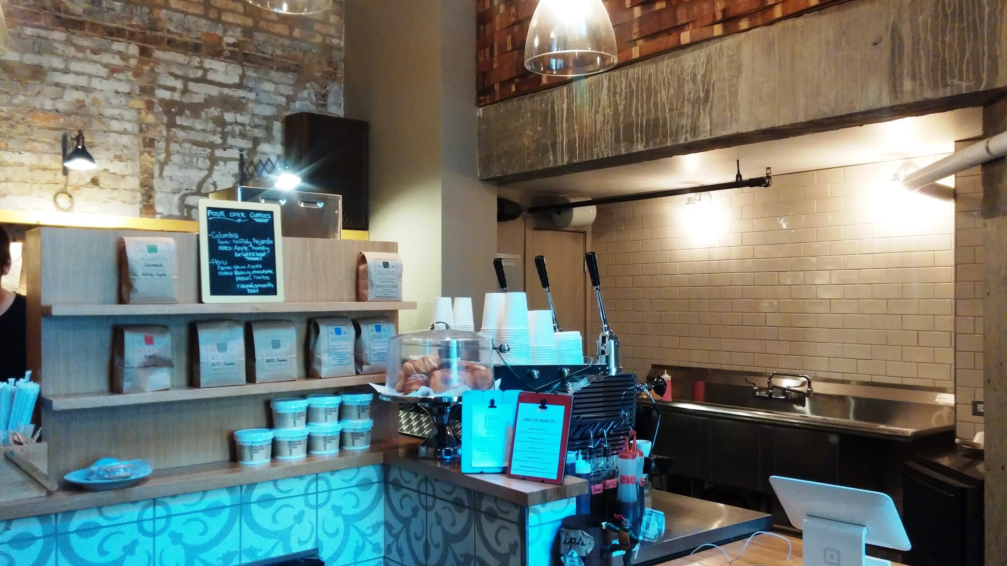 Espresso bar with patterned blue tile, bagged beans and pastry dome