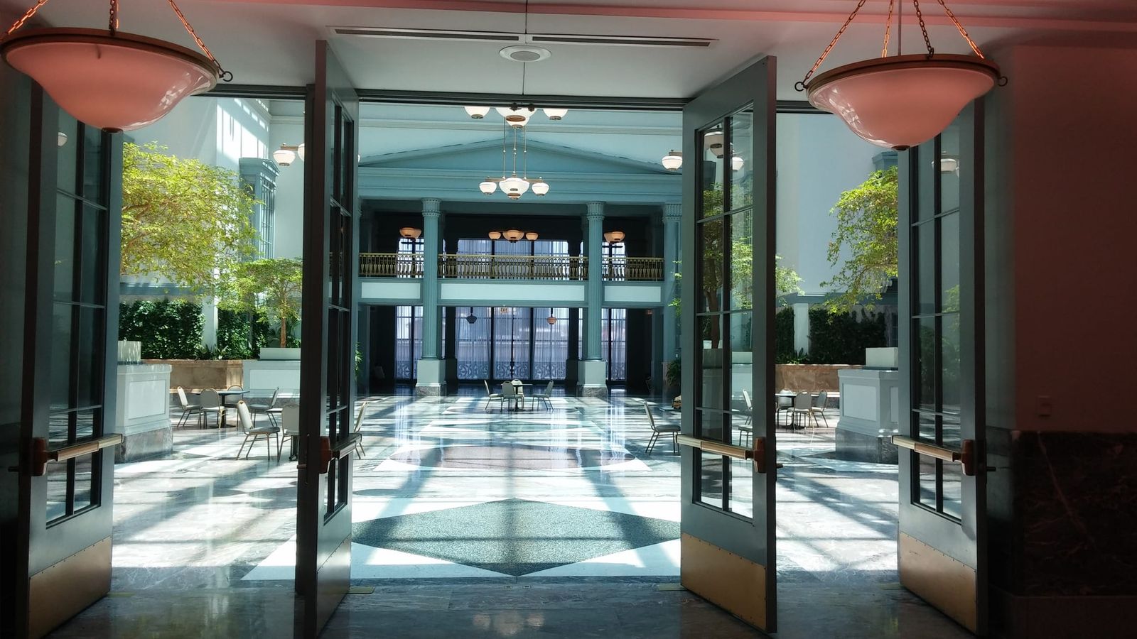 View through open glass doors onto a marble-floored atrium with tables