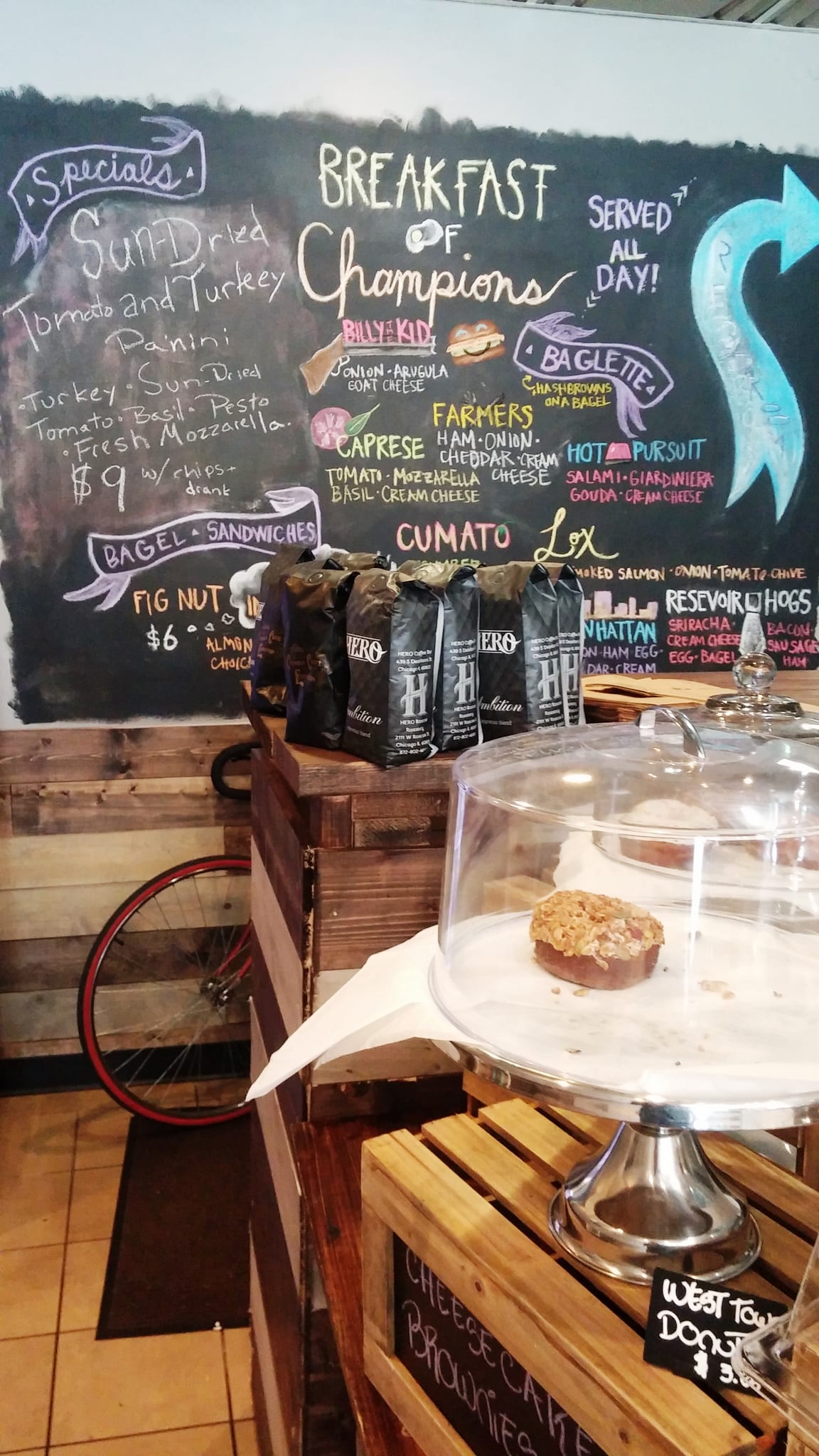 Chalkboard breakfast menu behind bagged coffee and a cake dome