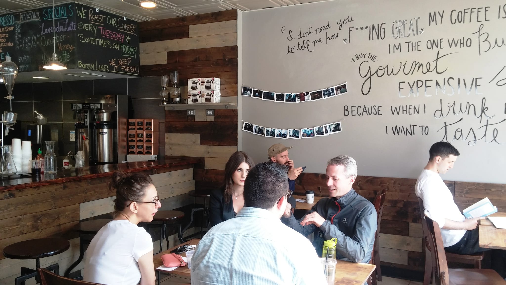 Customers at wooden tables beside a wall painted with a coffee quote