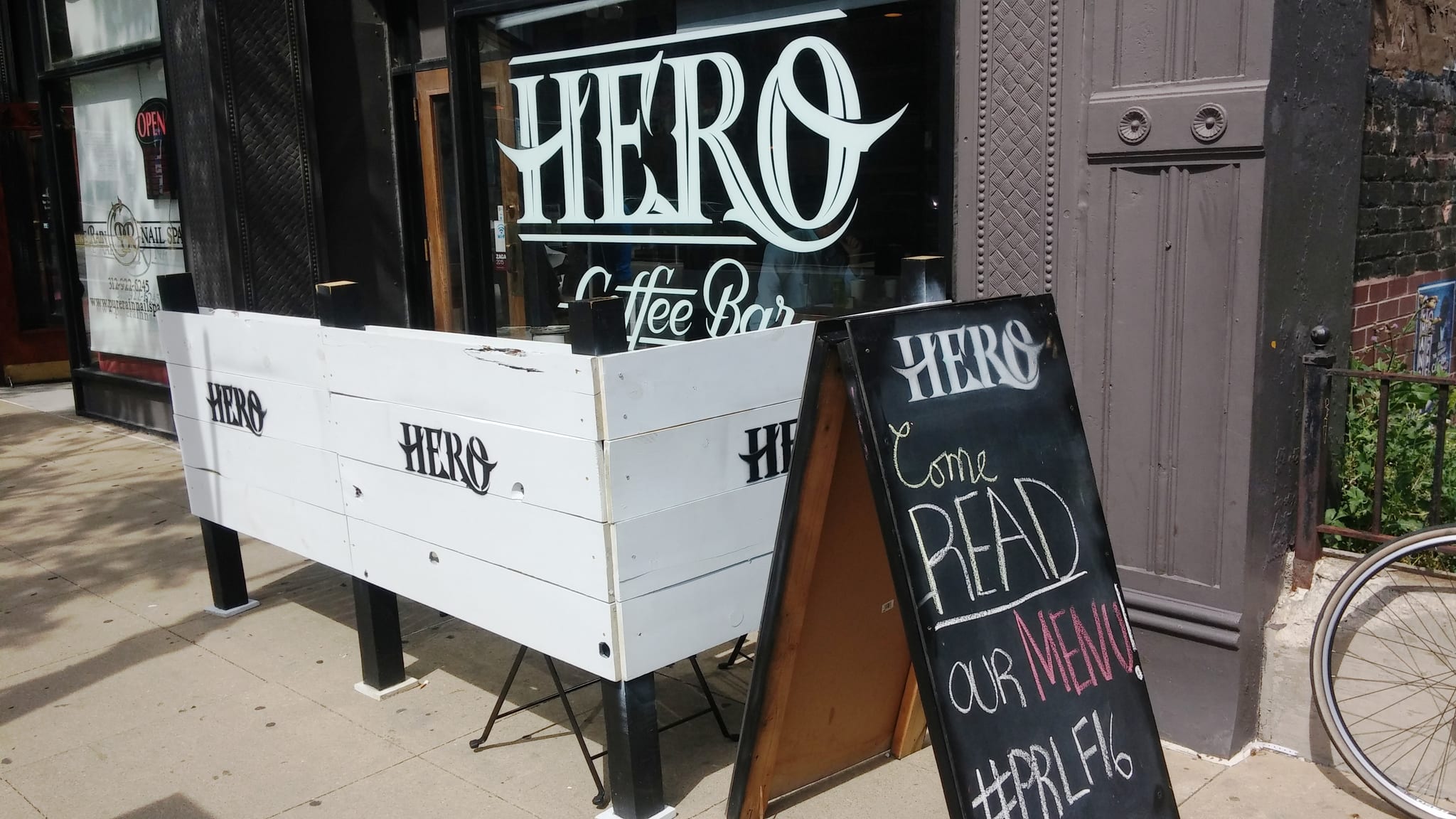 Sidewalk storefront with white planter barrier and a chalkboard A-frame sign
