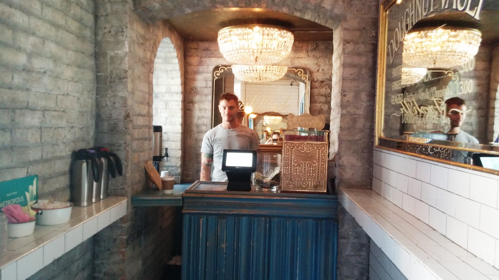 Barista behind a narrow brick-walled counter under a crystal chandelier