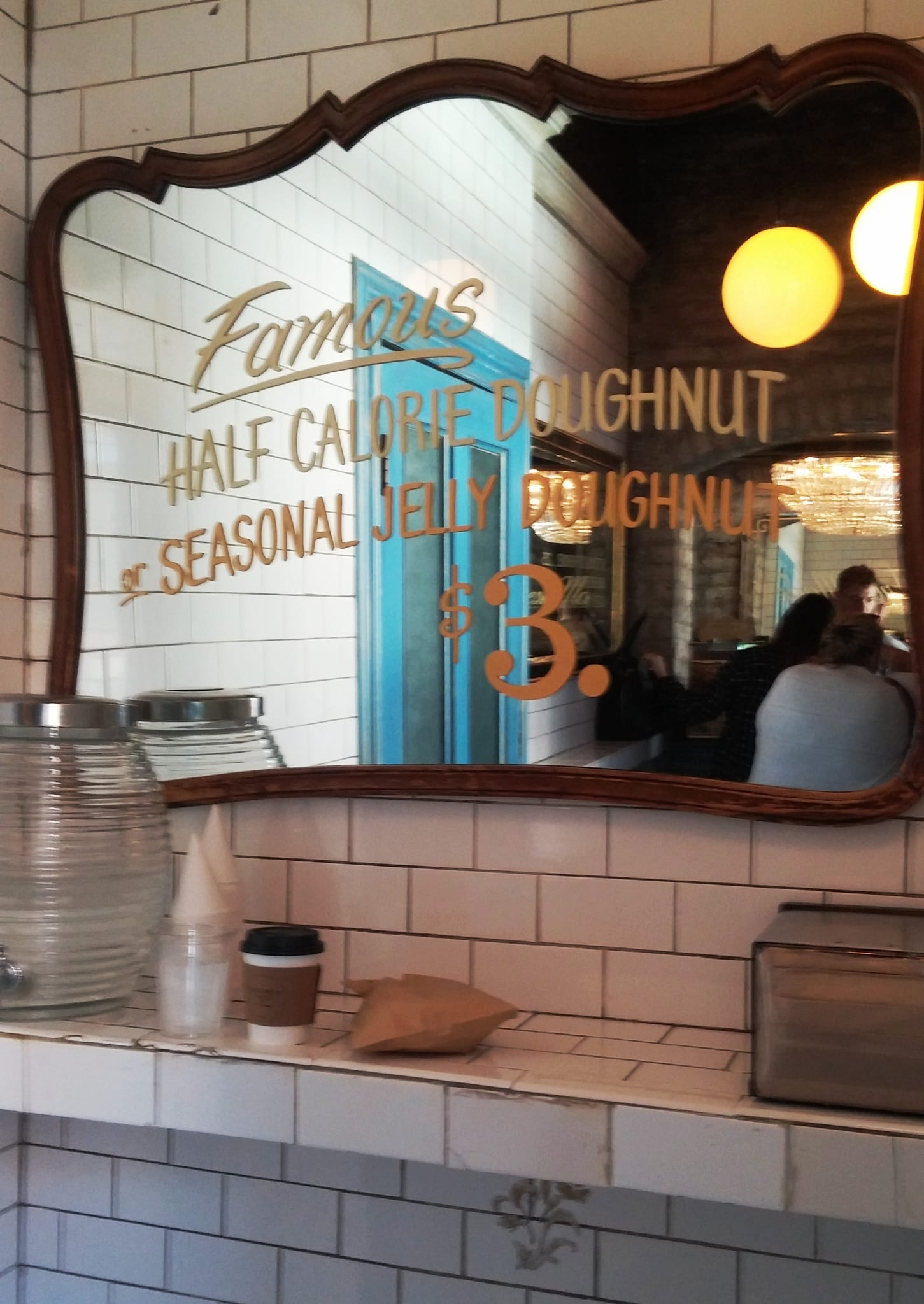 Gilt-framed mirror advertising doughnuts above a white subway-tiled ledge