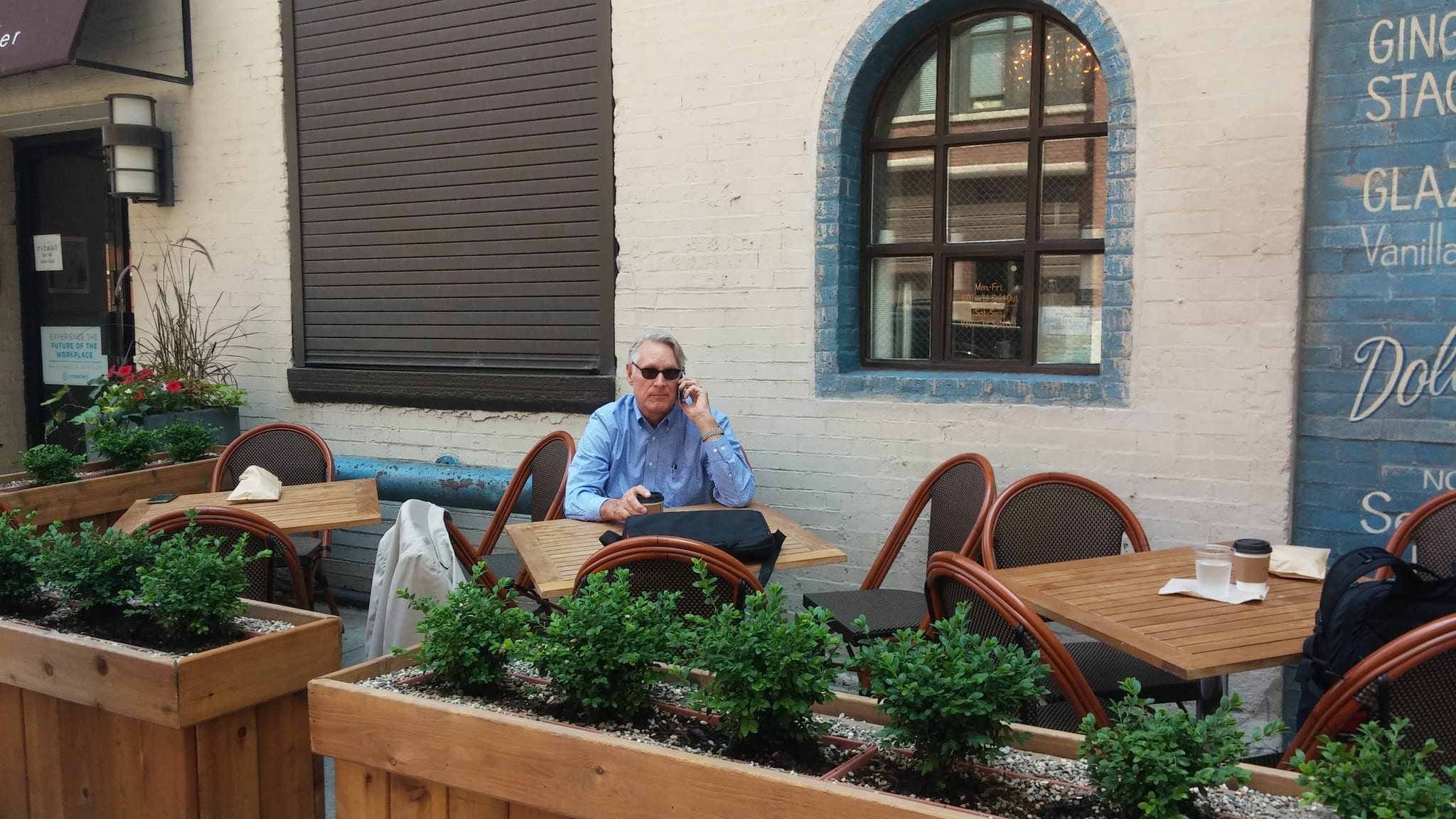 Man on his phone at a sidewalk patio table with coffee