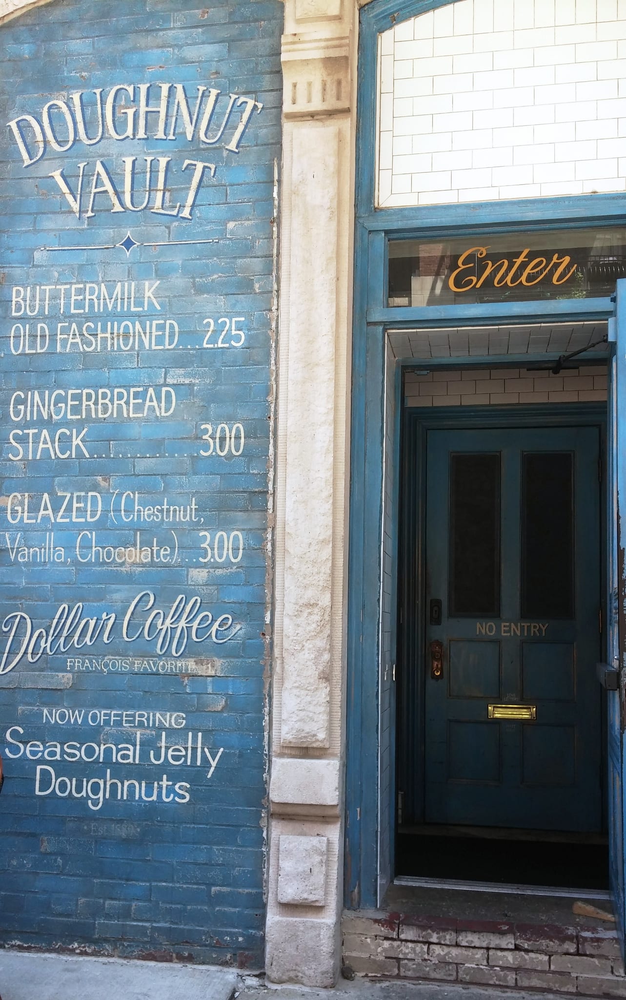 Blue brick wall painted with a doughnut menu beside an open door