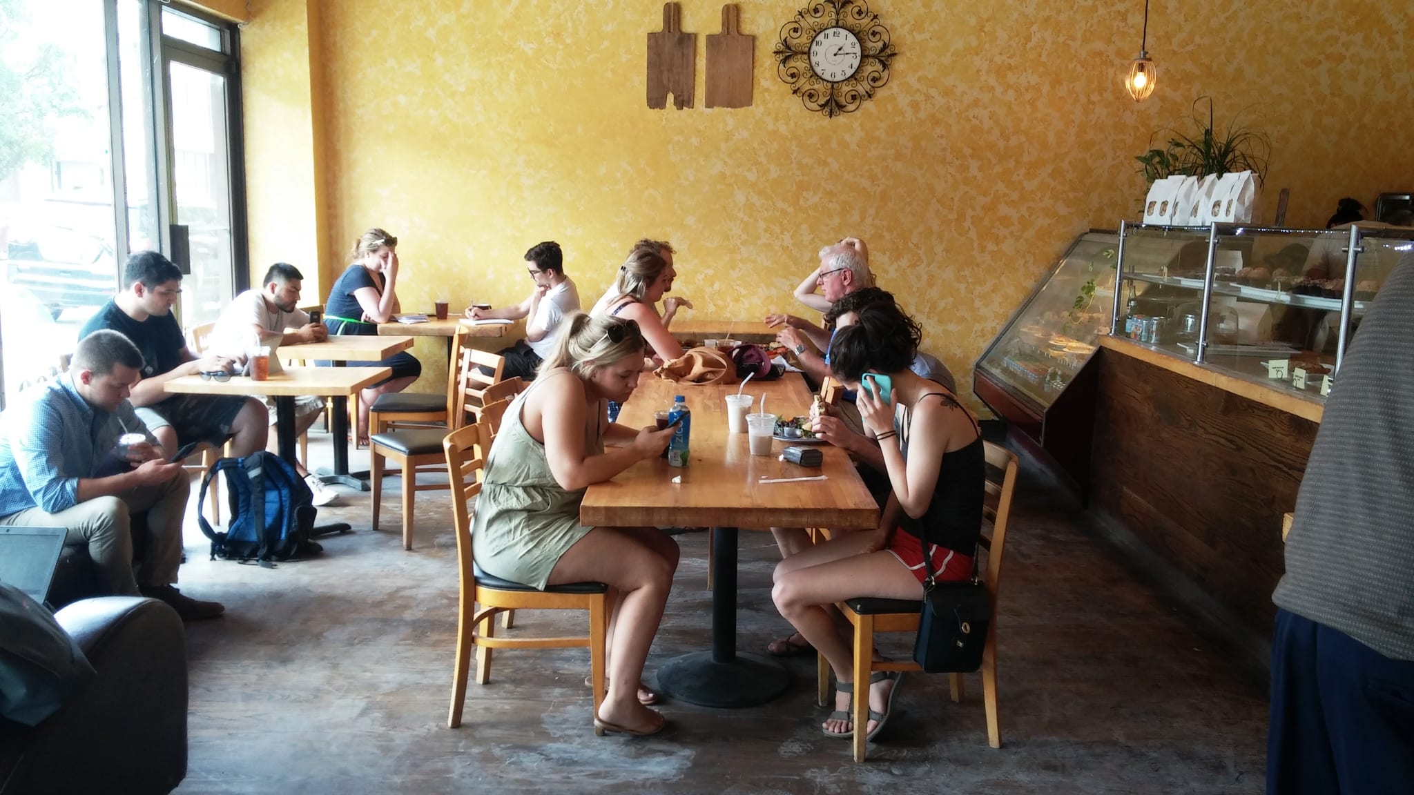 Busy yellow-walled cafe with wooden tables and a pastry display case