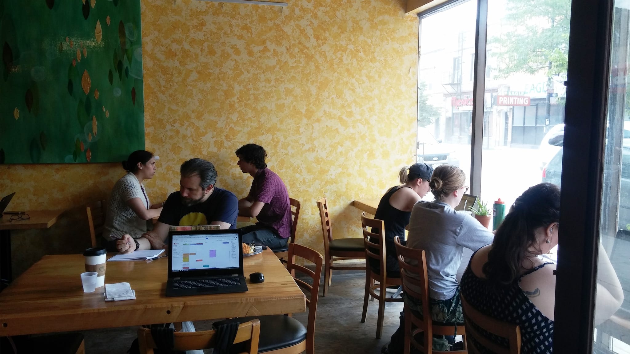 Cafe tables with laptops and coffee beside a bright street-facing window