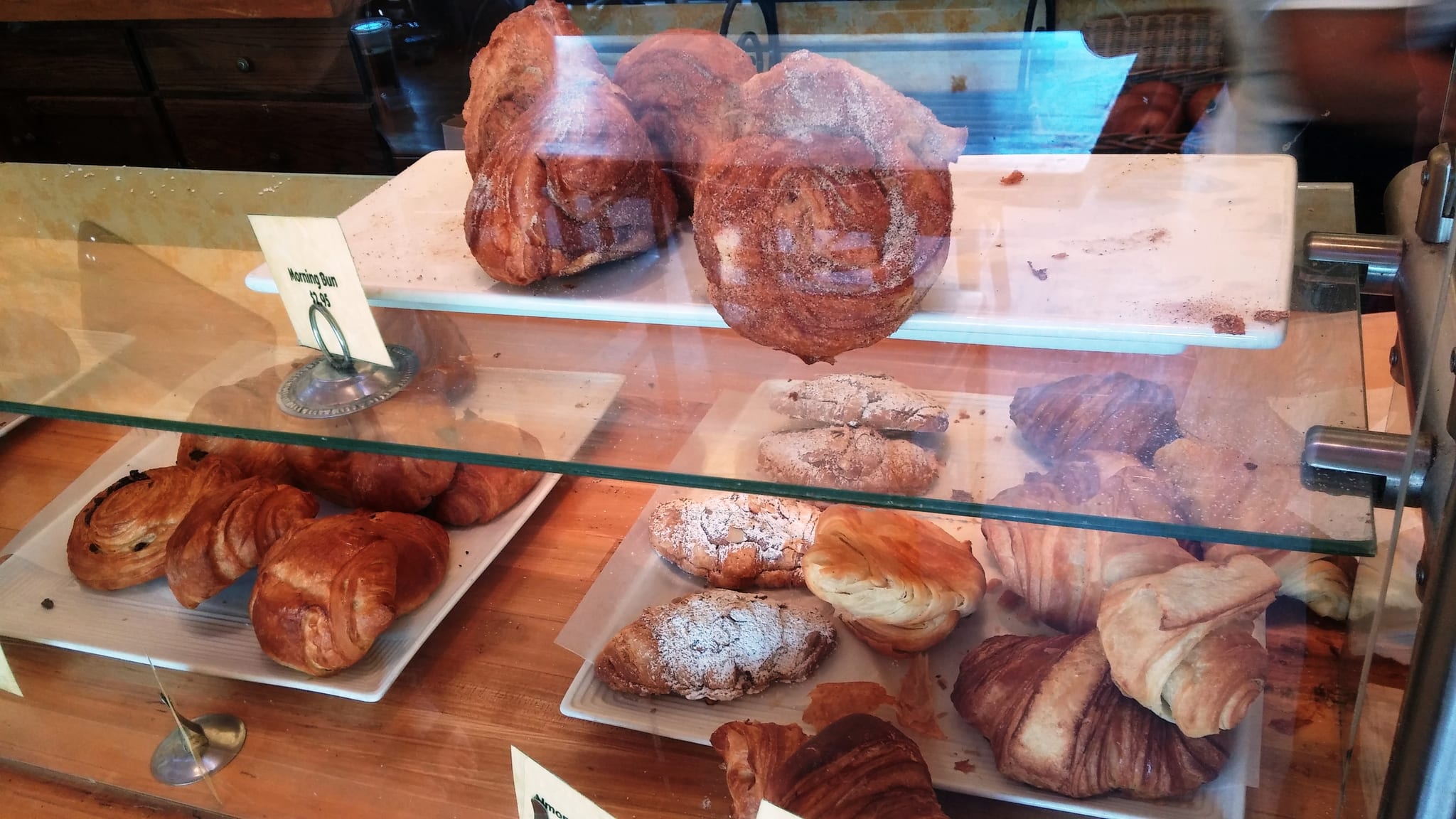 Pastry case with morning buns, croissants and almond pastries on trays