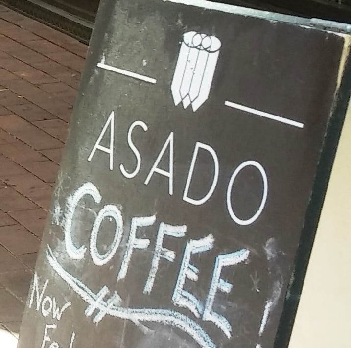 Chalkboard sidewalk sign lettered Asado Coffee beside brick pavement