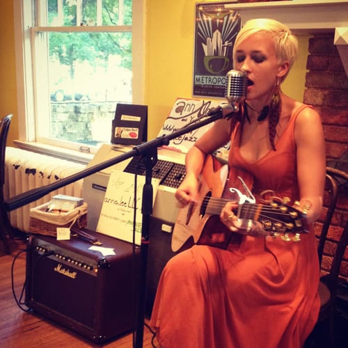 Singer in orange dress playing acoustic guitar beside Marshall amp