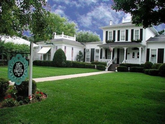 White clapboard house with lawn, hedges and hanging sign