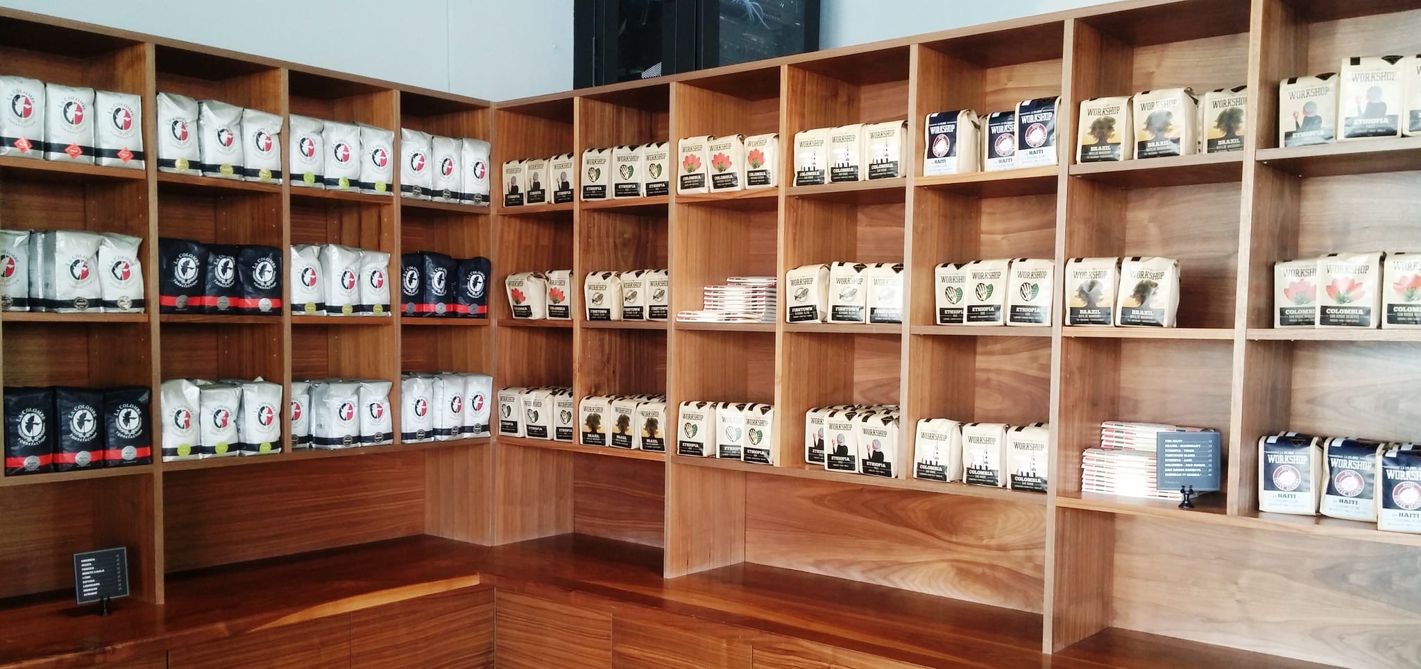 Wall of walnut shelving stocked with bags of whole bean coffee