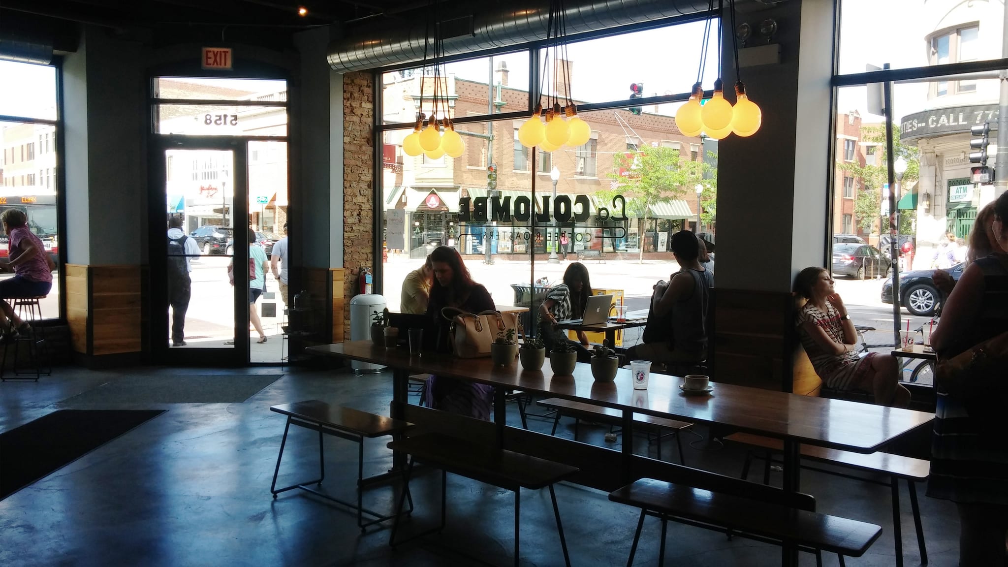 Corner cafe with long wood communal tables, benches and glowing bulbs