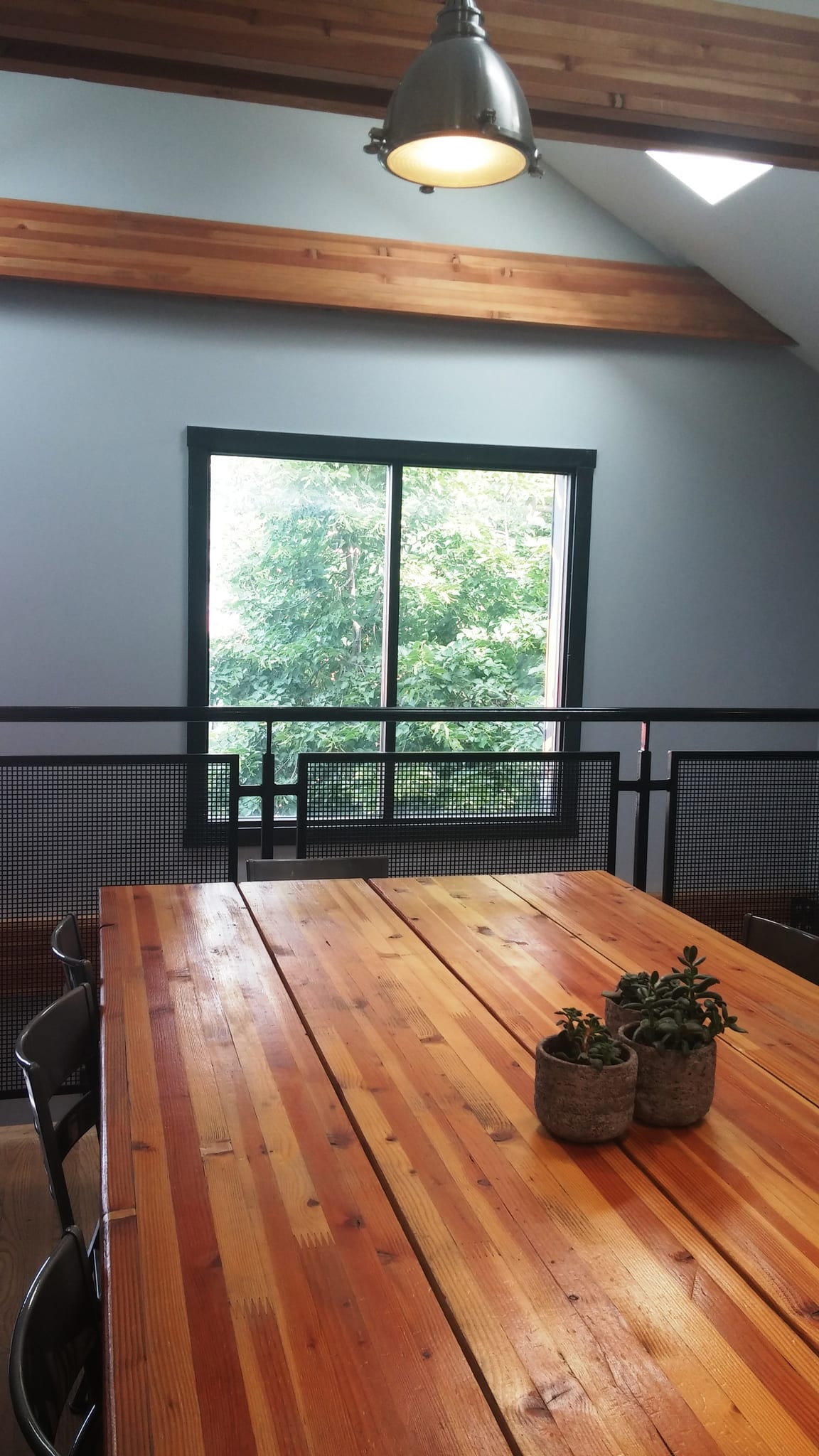 Reclaimed-wood communal table under exposed beams beside a leafy window