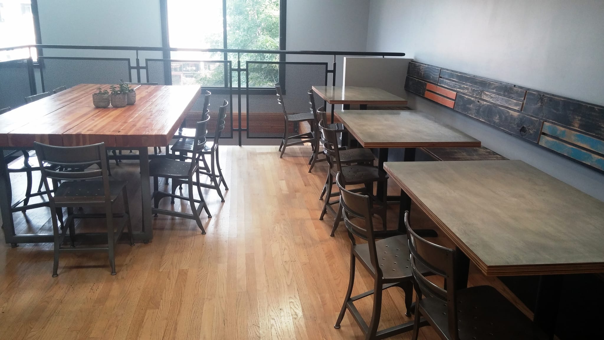Upstairs seating with metal chairs, communal table and wall-side two-tops