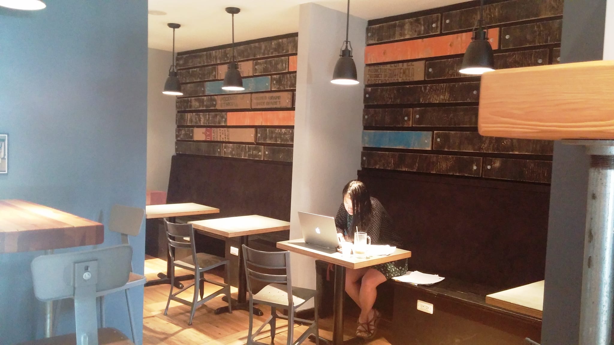 Cafe seating with reclaimed coffee-crate wall and woman working on a laptop