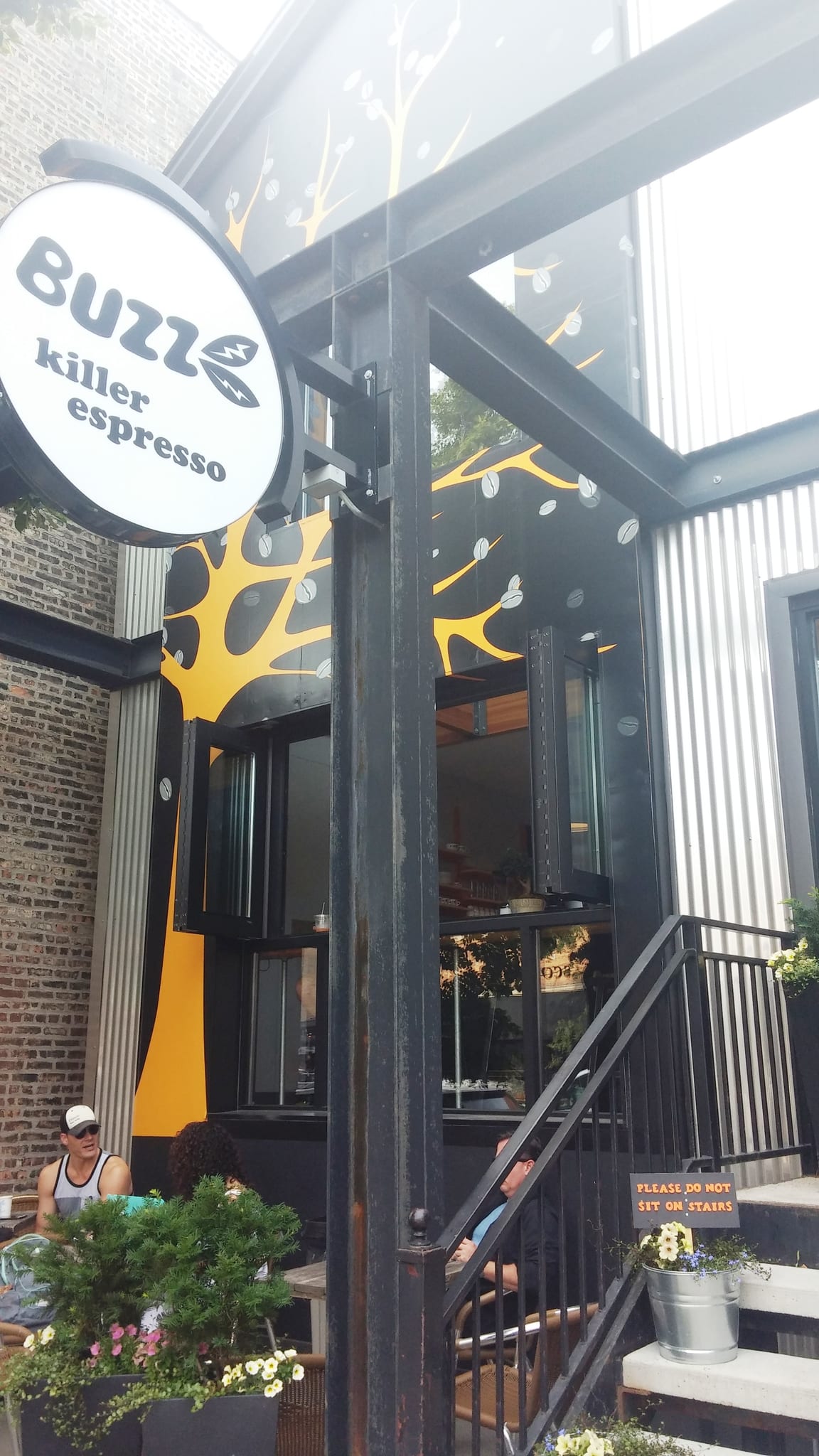 Storefront with yellow tree mural, open windows and sidewalk patio seating