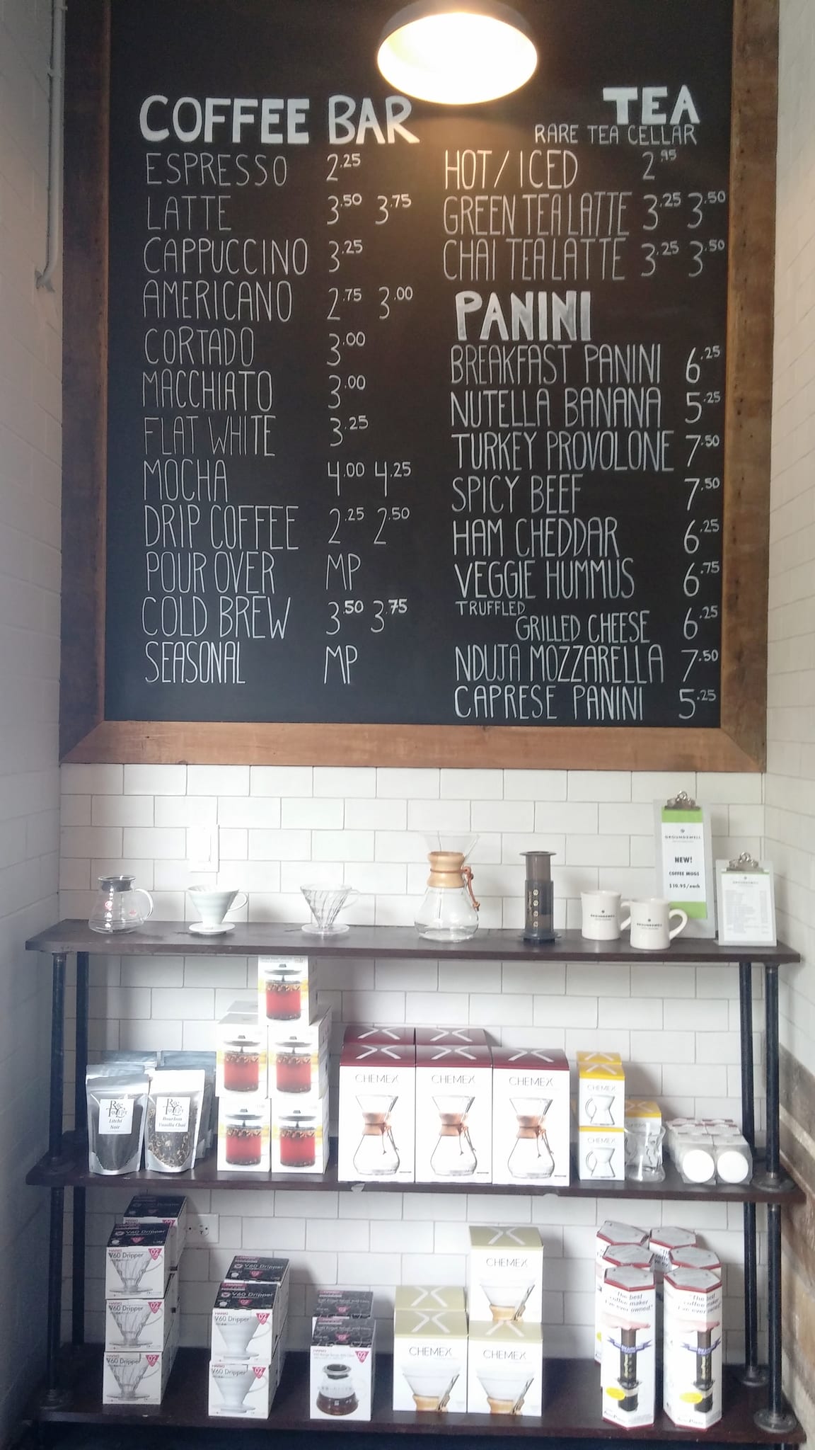 Chalkboard coffee and panini menu above shelves of Chemex and V60 brewers