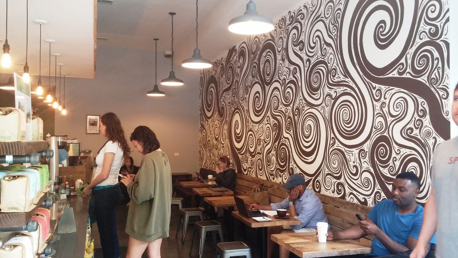 Busy cafe with bold black-and-white swirl mural and wooden bench tables
