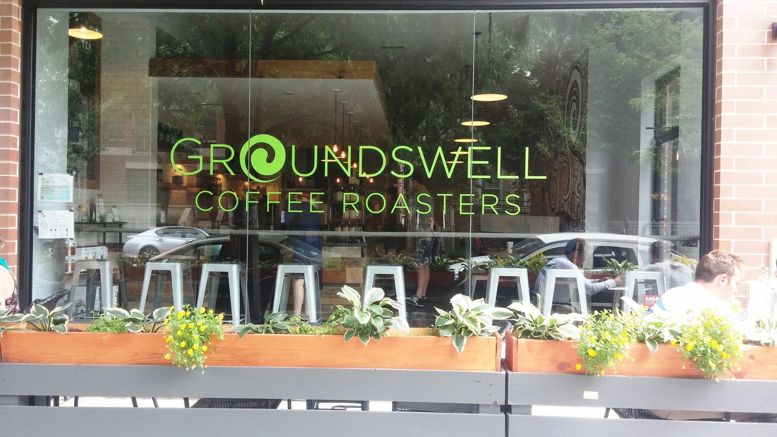 Storefront window with green Groundswell Coffee Roasters lettering and flower boxes