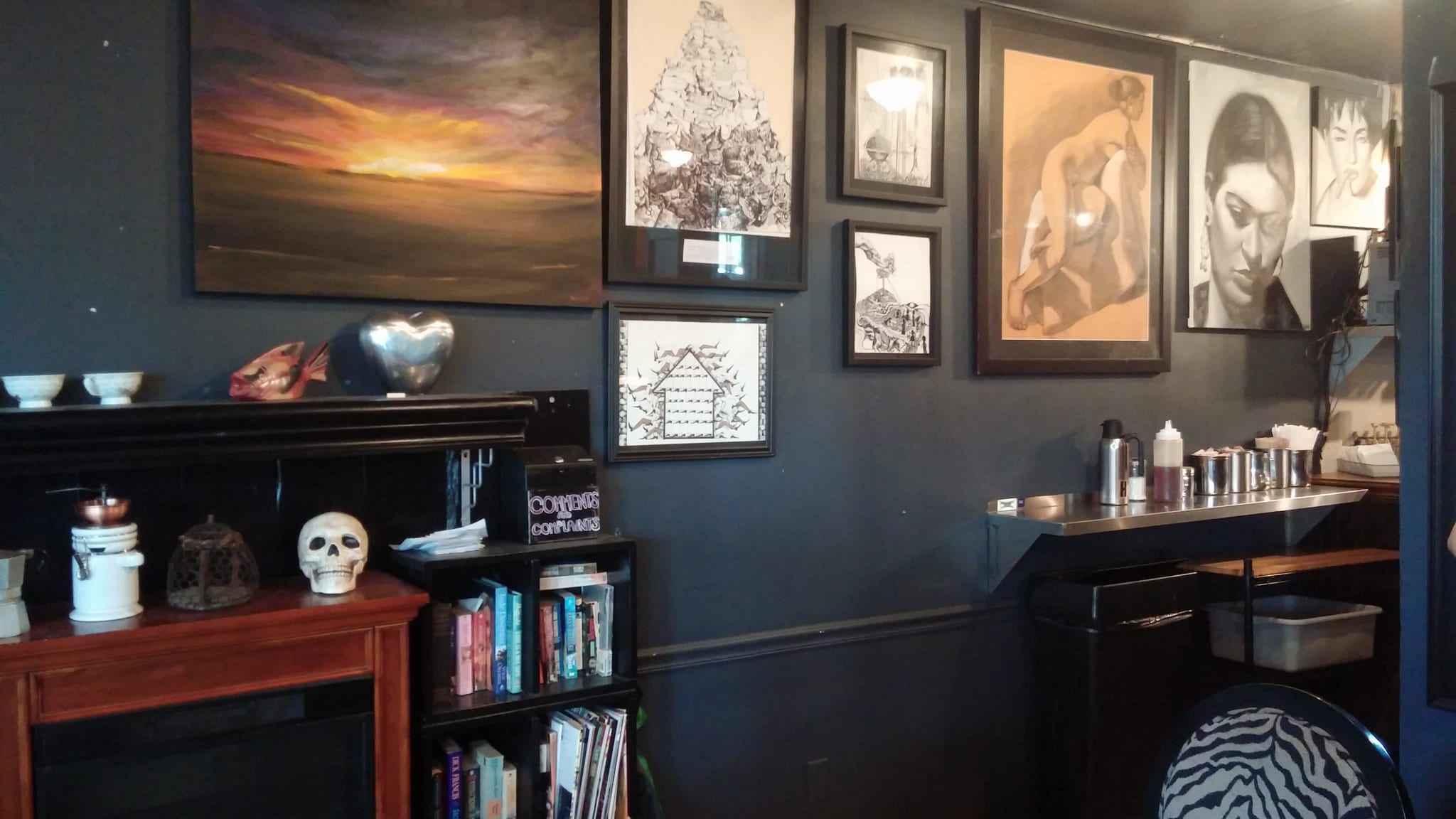 Dark wall hung with paintings and drawings above a mantel and milk station