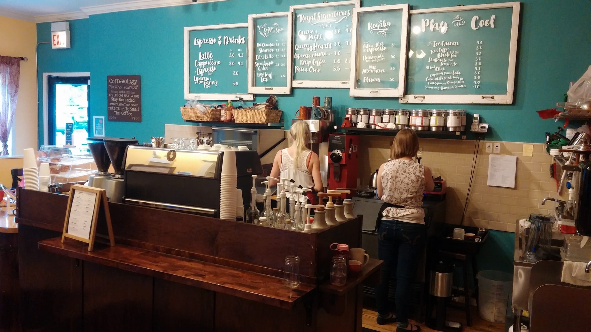 Teal wall of chalk menu boards above espresso machine and wooden counter
