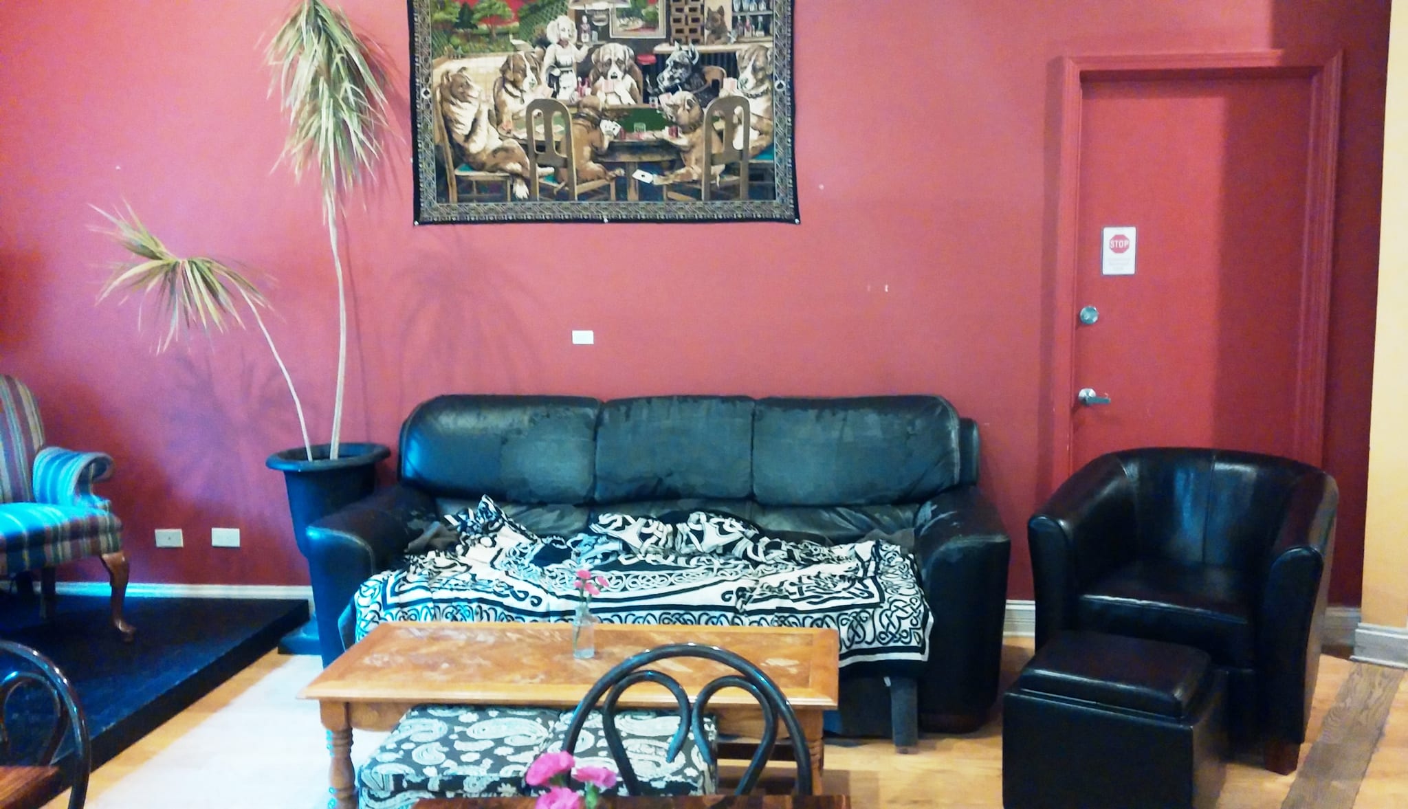 Black leather couch and armchair against red wall with dogs-playing-cards tapestry
